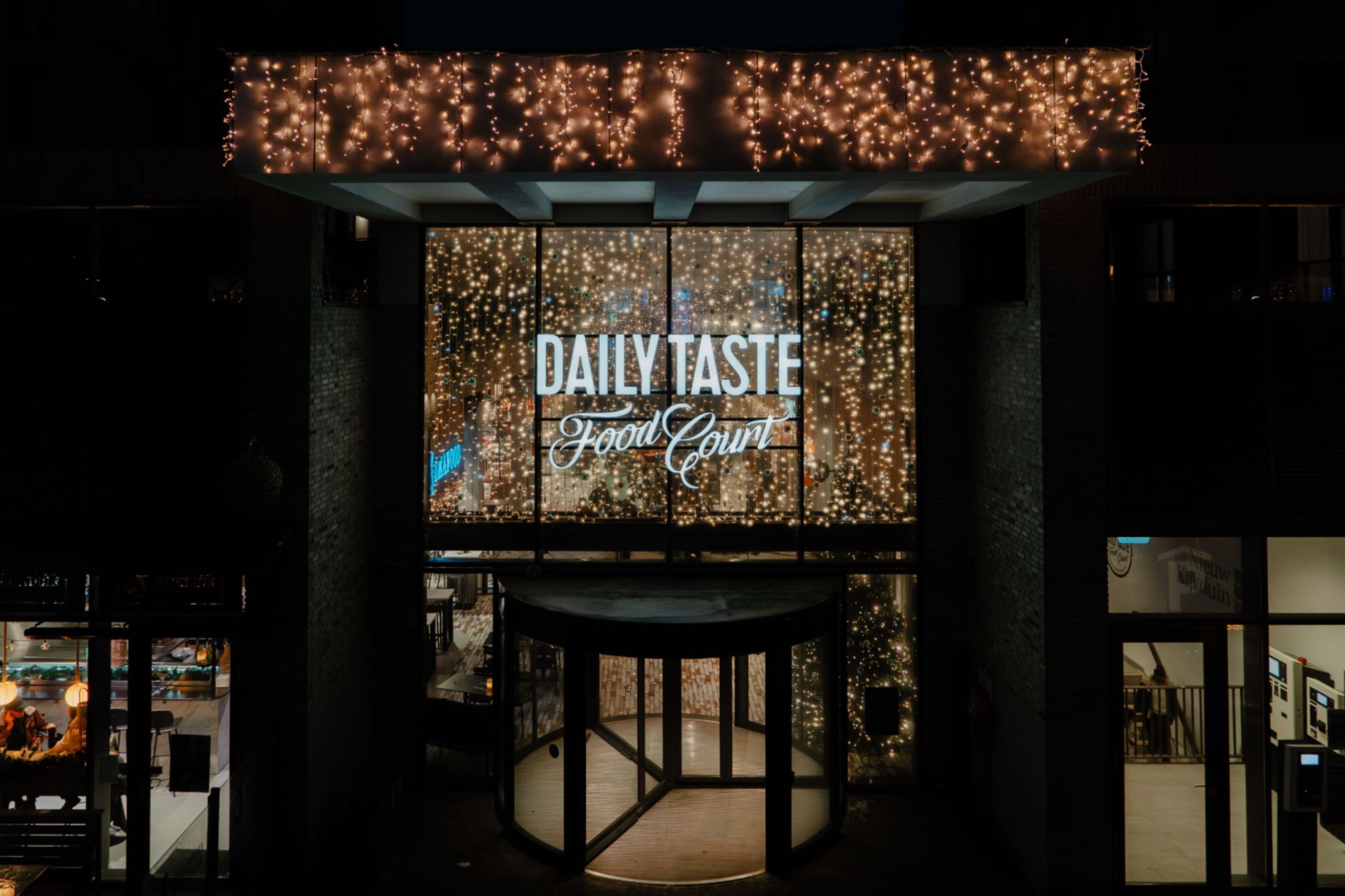 Verlichte ingang van Daily Taste Food Court gerund door retail ondernemers in Nieuw Kijkduin.